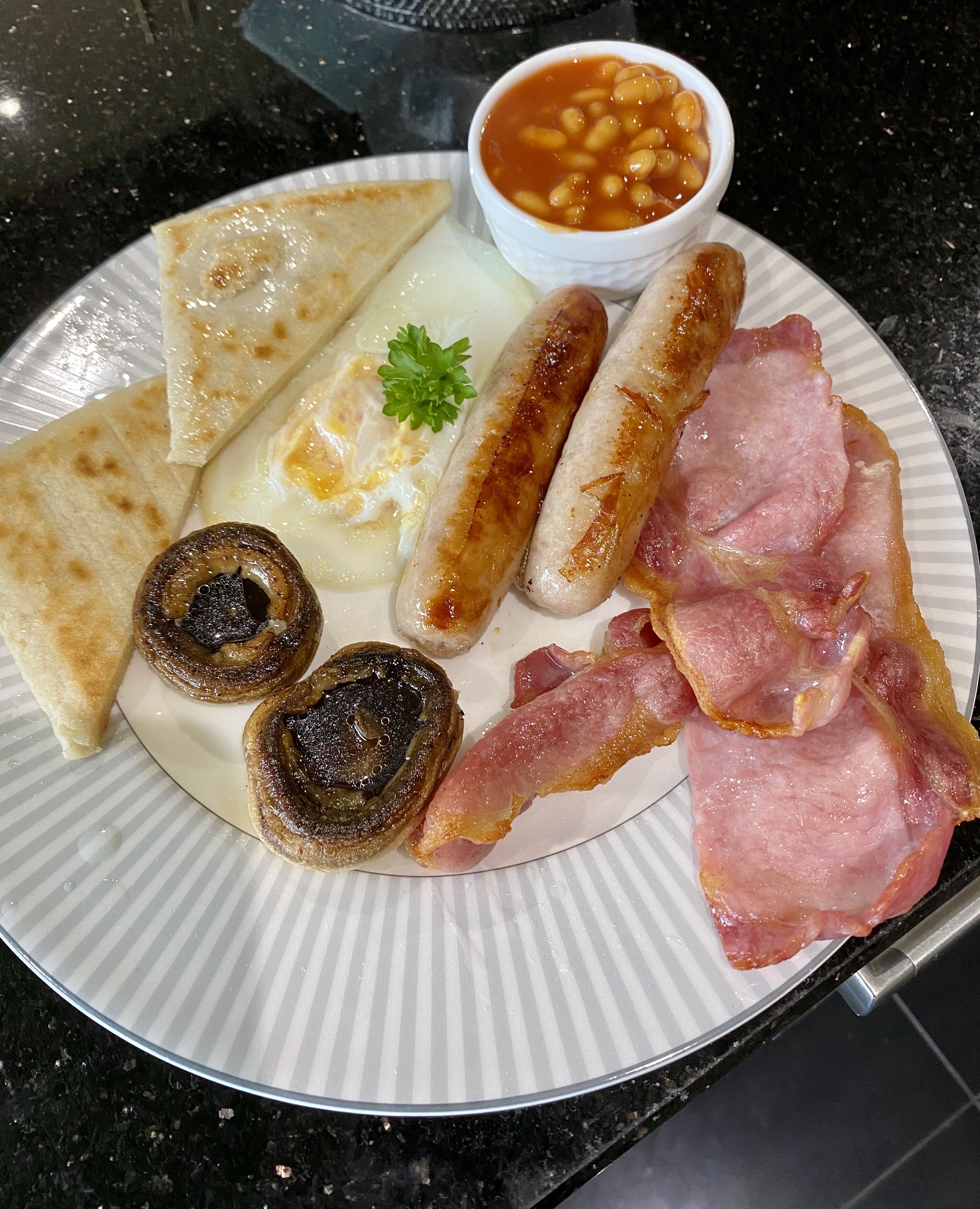 A plate of breakfast food including eggs, sausages, bacon, toast, mushrooms, and beans.