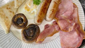 A plate of breakfast food including eggs, sausages, bacon, toast, mushrooms, and beans.