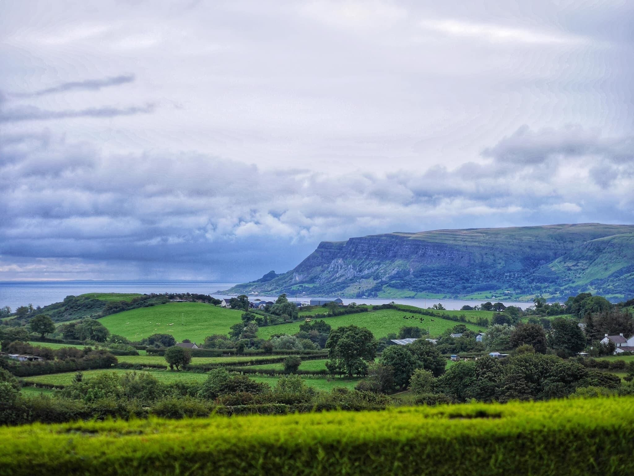 A rural landscape with rolling hills, a body of water, and a mountain in the distance.
