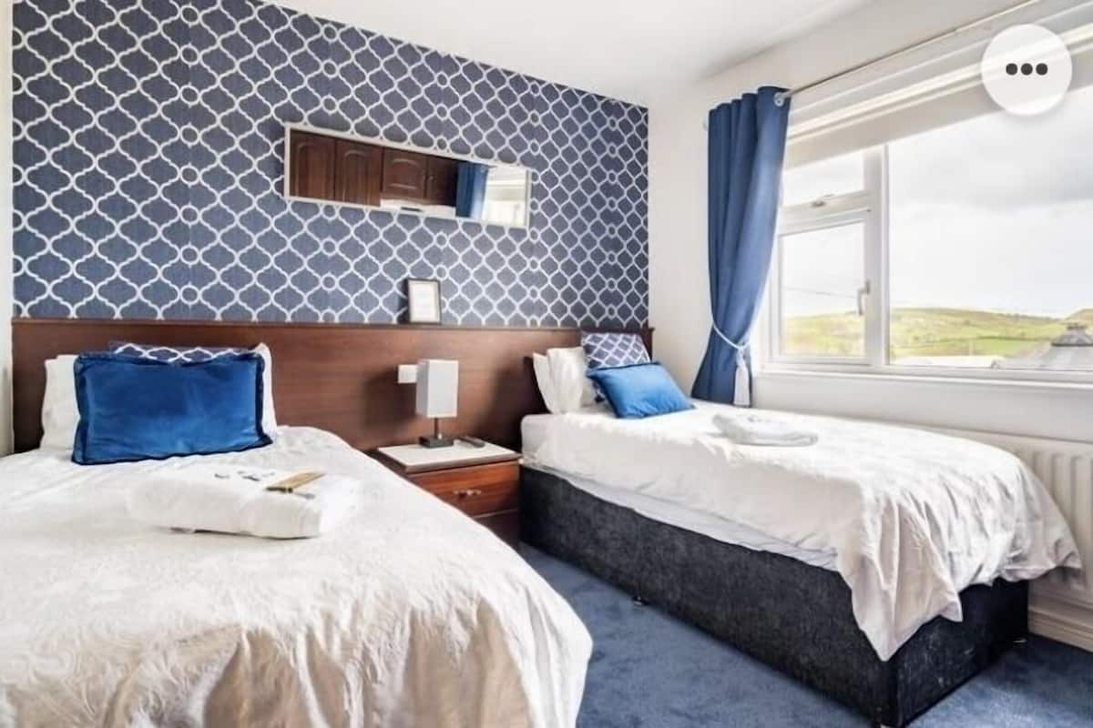 A hotel room with two beds, a wooden headboard, a nightstand, a mirror, and a window with a view of the countryside.