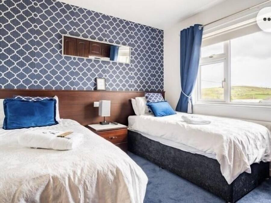 A hotel room with two beds, a wooden headboard, a nightstand, a mirror, and a window with a view of the countryside.