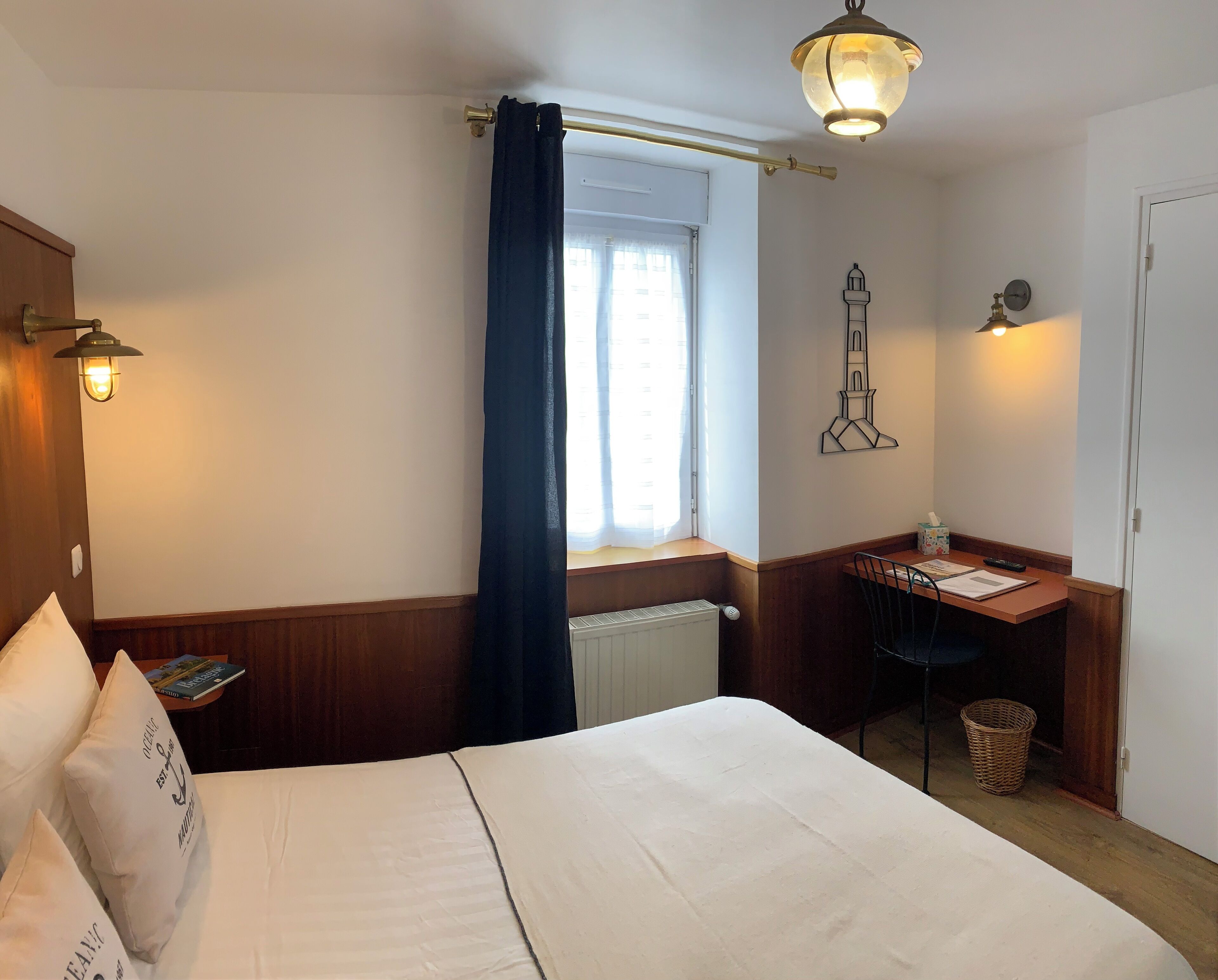 Ein Hotelzimmer mit Bett, Schreibtisch, Fenster mit Vorhängen, einer Wandlampe und einer Wanddekoration.
