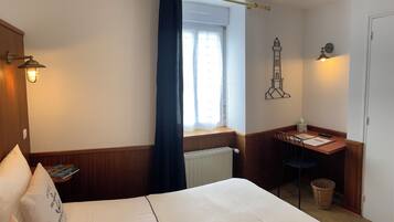 Ein Hotelzimmer mit Bett, Schreibtisch, Fenster mit Vorhängen, einer Wandlampe und einer Wanddekoration.