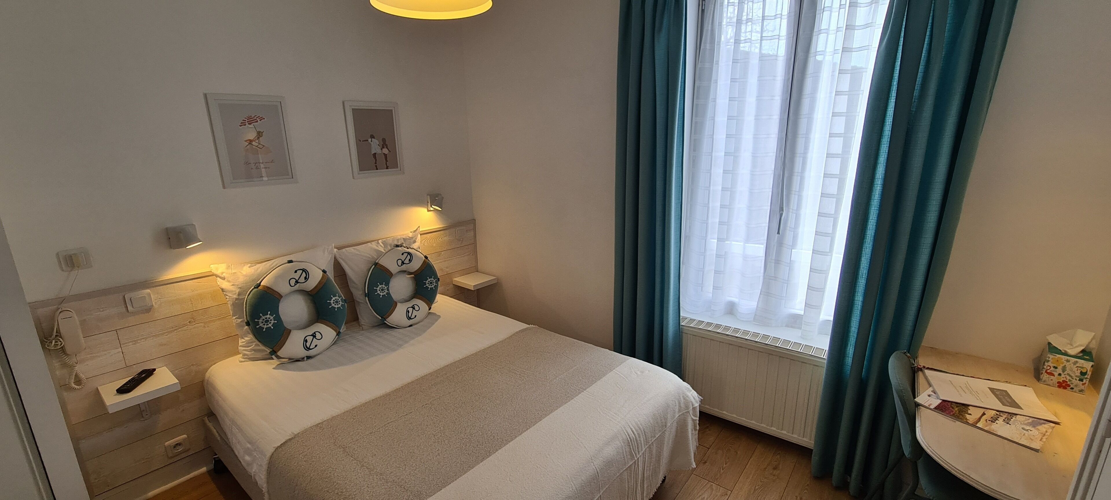 Et hotelværelse med seng, sengeborde, et vindue med gardiner og billedkunst på væggen.