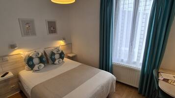 Et hotelværelse med seng, sengeborde, et vindue med gardiner og billedkunst på væggen.
