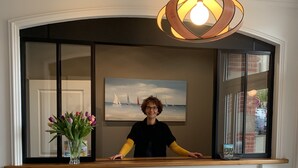 A reception desk with a wooden top, a vase of flowers, and a painting of sailboats on the wall behind. - Hotel de France (Pleneuf-Val-Andre)