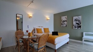A room with a bed, a dining table with chairs, a laptop, and a hanging light fixture. - Hotel de France (Pleneuf-Val-Andre)