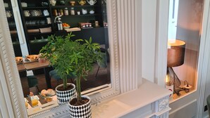 A dining area with a white fireplace, a potted plant, and a table set with a lamp and a tray of food. - Hotel de France (Pleneuf-Val-Andre)
