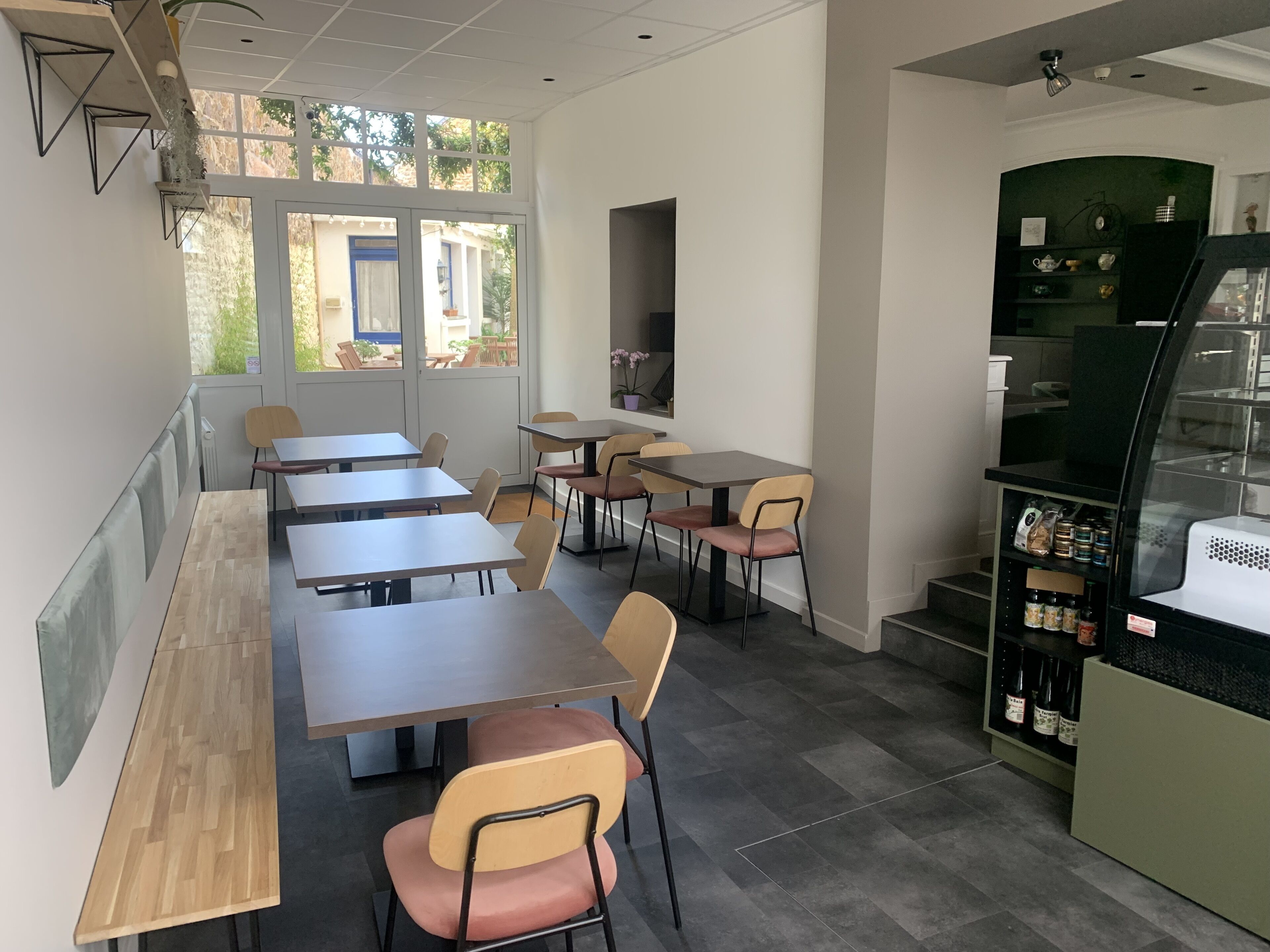 Um café moderno com várias mesas e cadeiras, janelas amplas e um balcão com bebidas.