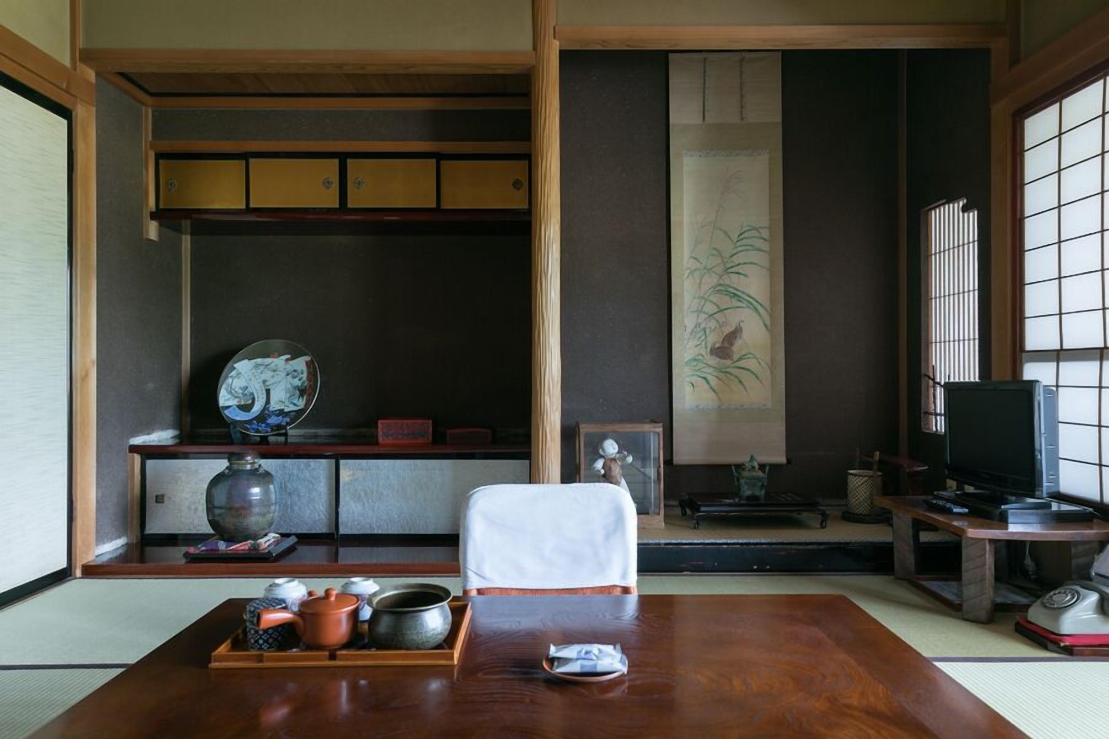 A traditional Japanese room with tatami flooring, a low table with tea utensils, a television, and sliding doors.