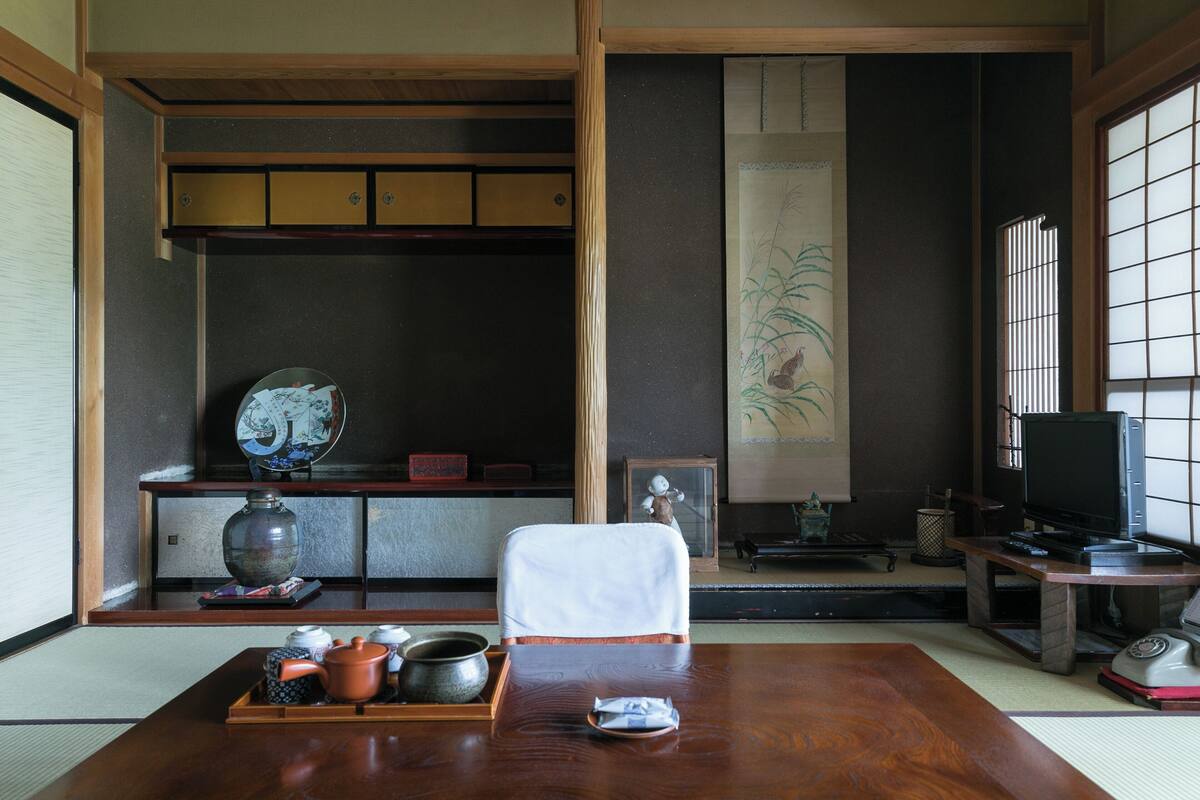 A traditional Japanese room with tatami flooring, a low table with tea utensils, a television, and sliding doors.