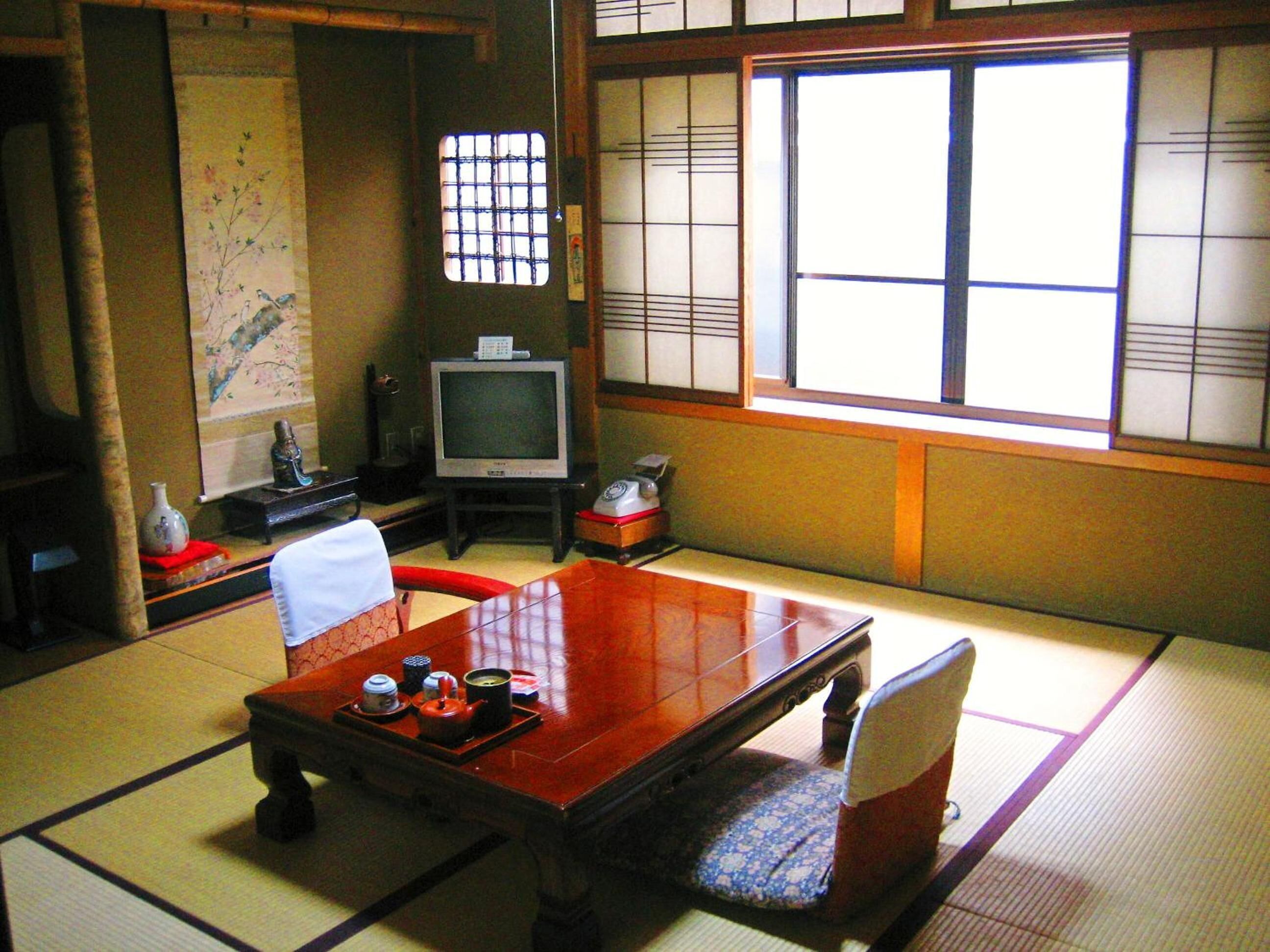 Une pièce de style japonais traditionnel, avec un sol recouvert de tatamis, une petite table basse avec un service à thé, un téléviseur et des portes coulissantes.