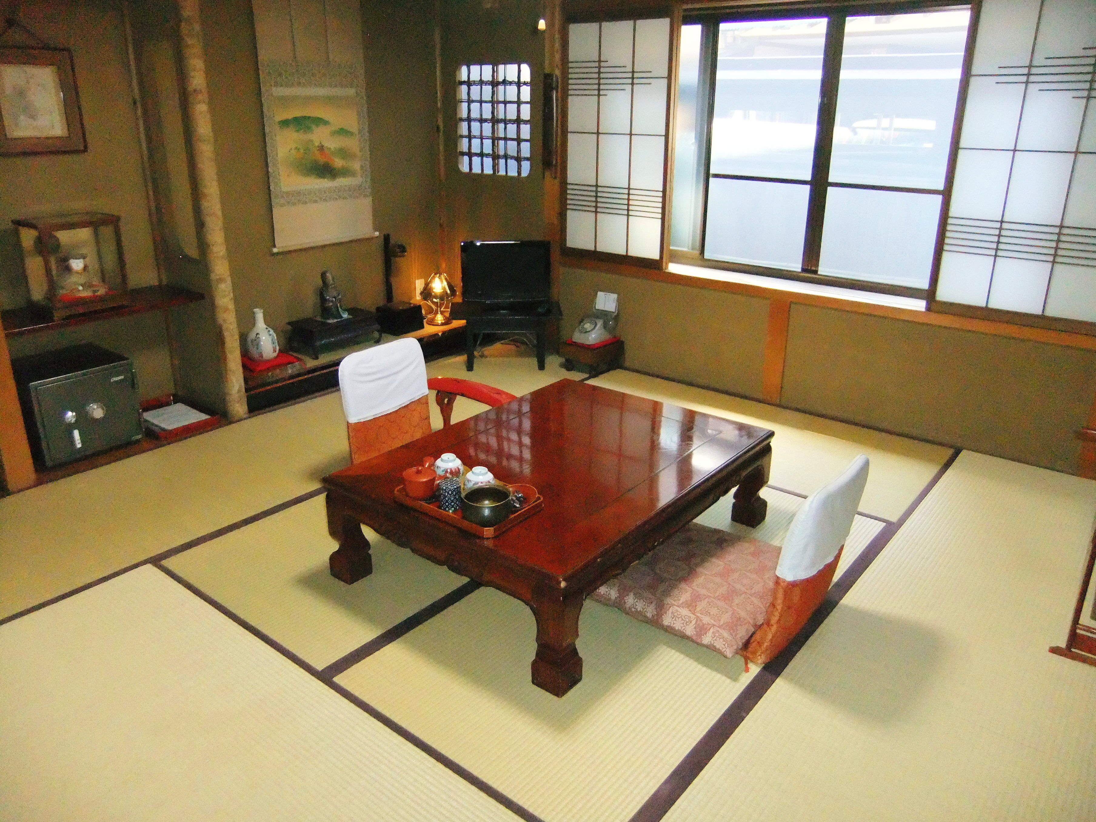 A traditional Japanese tatami room with a wooden table, tatami mats, a shoji screen, and a view of the outside.