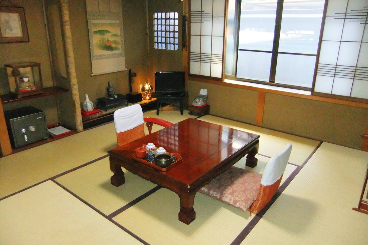 A traditional Japanese tatami room with a wooden table, tatami mats, a shoji screen, and a view of the outside.