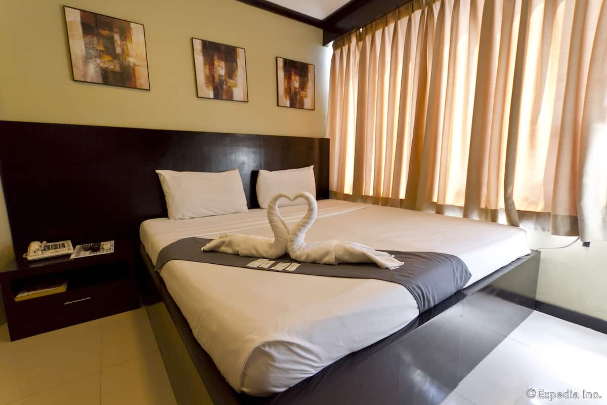 A hotel room with a large bed, a headboard, a nightstand, and a window with curtains.