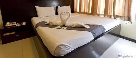 A hotel room with a large bed, a headboard, a nightstand, and a window with curtains.