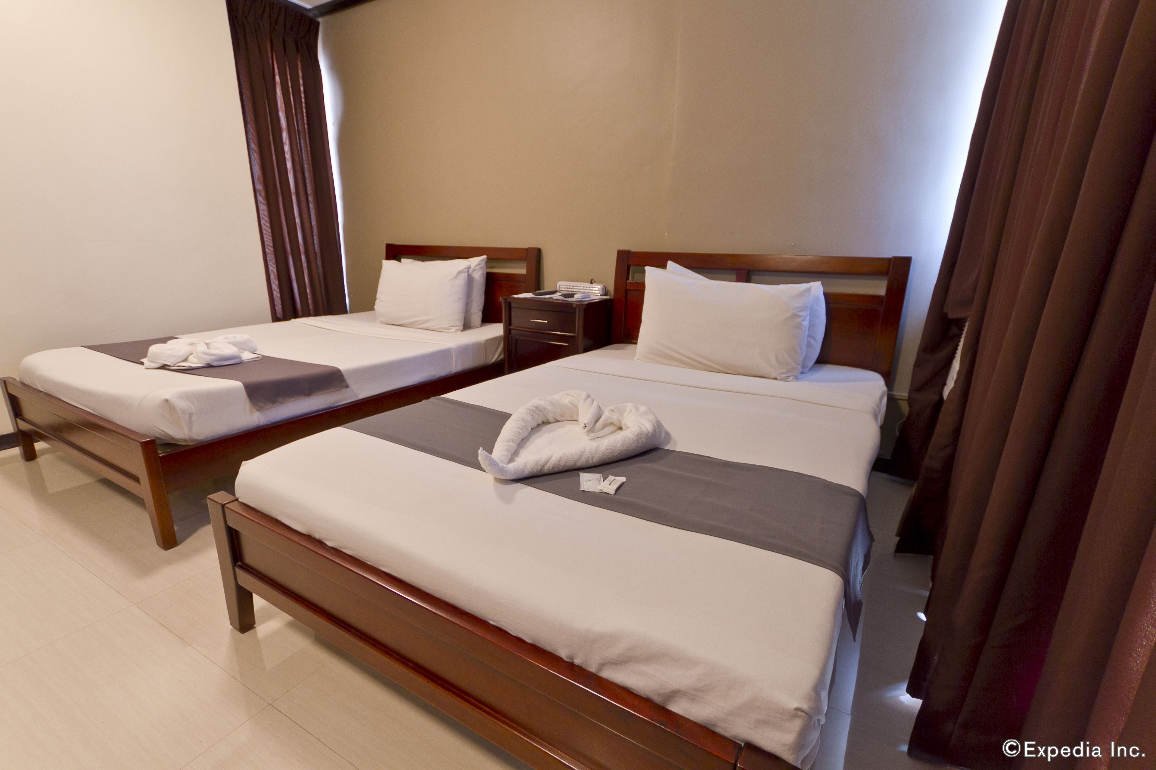A hotel room with two single beds, wooden headboards, and a nightstand with a lamp.