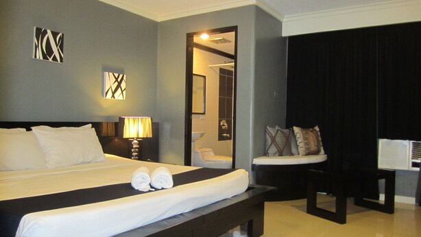 A hotel room with a large bed, a bedside table with a lamp, a chair, and a desk with a computer. - Richmond Plaza Hotel (Cebu City)