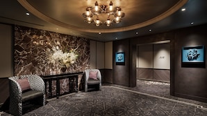 A lobby with a marble wall, a chandelier, two patterned chairs, a console table, and framed pictures on the walls. - Hotel Sosei Sapporo - MGallery Collection (Sapporo)