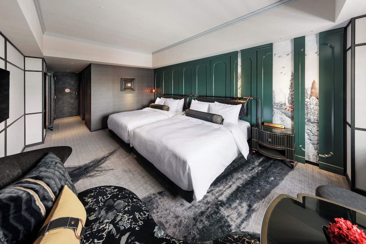 A modern hotel room with a large bed, a seating area, and a painting on the wall.