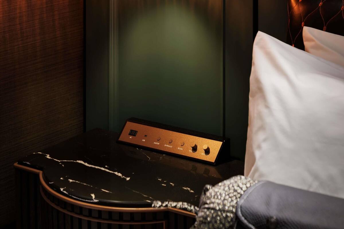 A room with a bed, a nightstand with a control panel, and a wall with a textured pattern.