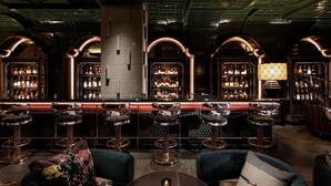 A bar area with multiple stools, a bar counter, and shelves stocked with bottles. - Hotel Sosei Sapporo - MGallery Collection (Sapporo)