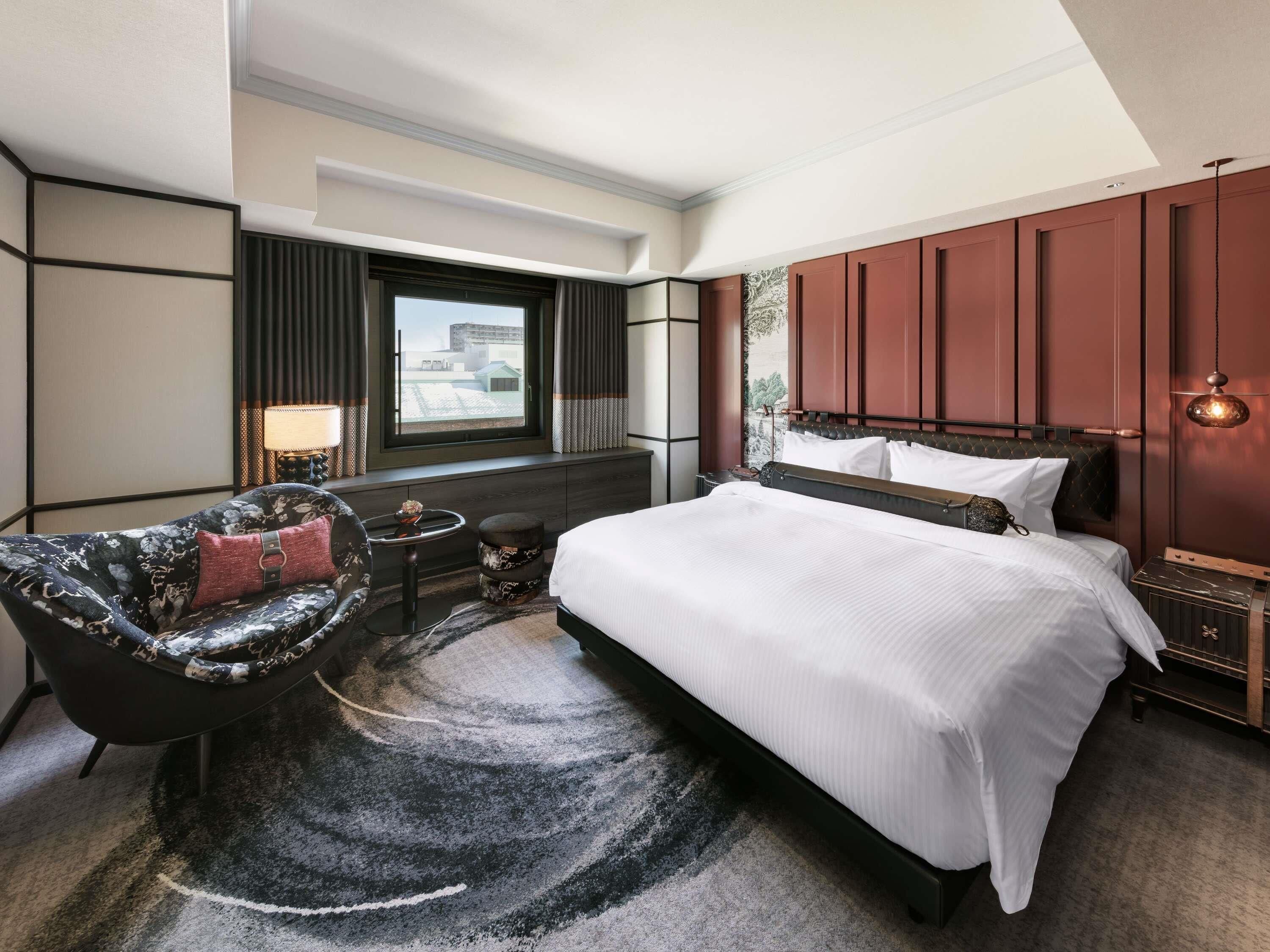 Une chambre d’hôtel avec un lit, un canapé, une petite table, une lampe et une fenêtre donnant sur un beau paysage.