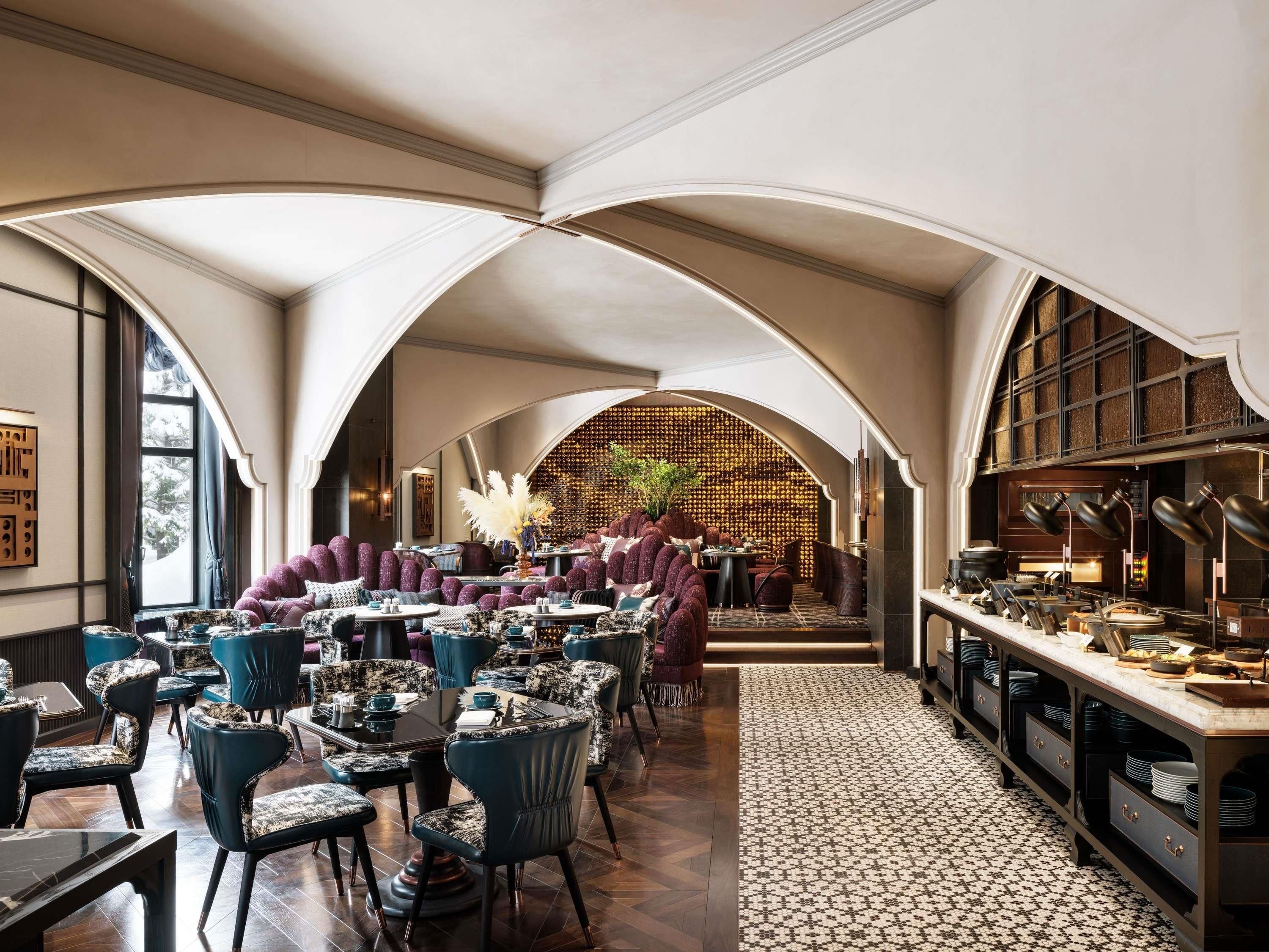 A restaurant with high arched ceilings, a central seating area with round tables and chairs, and a long counter with dishes.