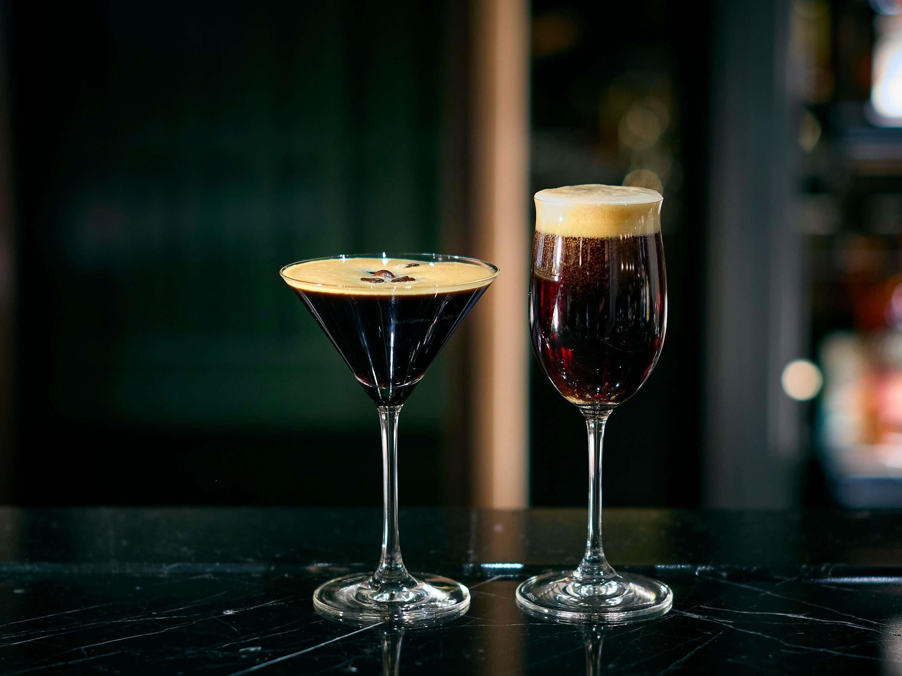 Dos vasos de bebidas oscuras sobre una superficie reflectante.