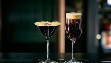 Dos vasos de bebidas oscuras sobre una superficie reflectante.