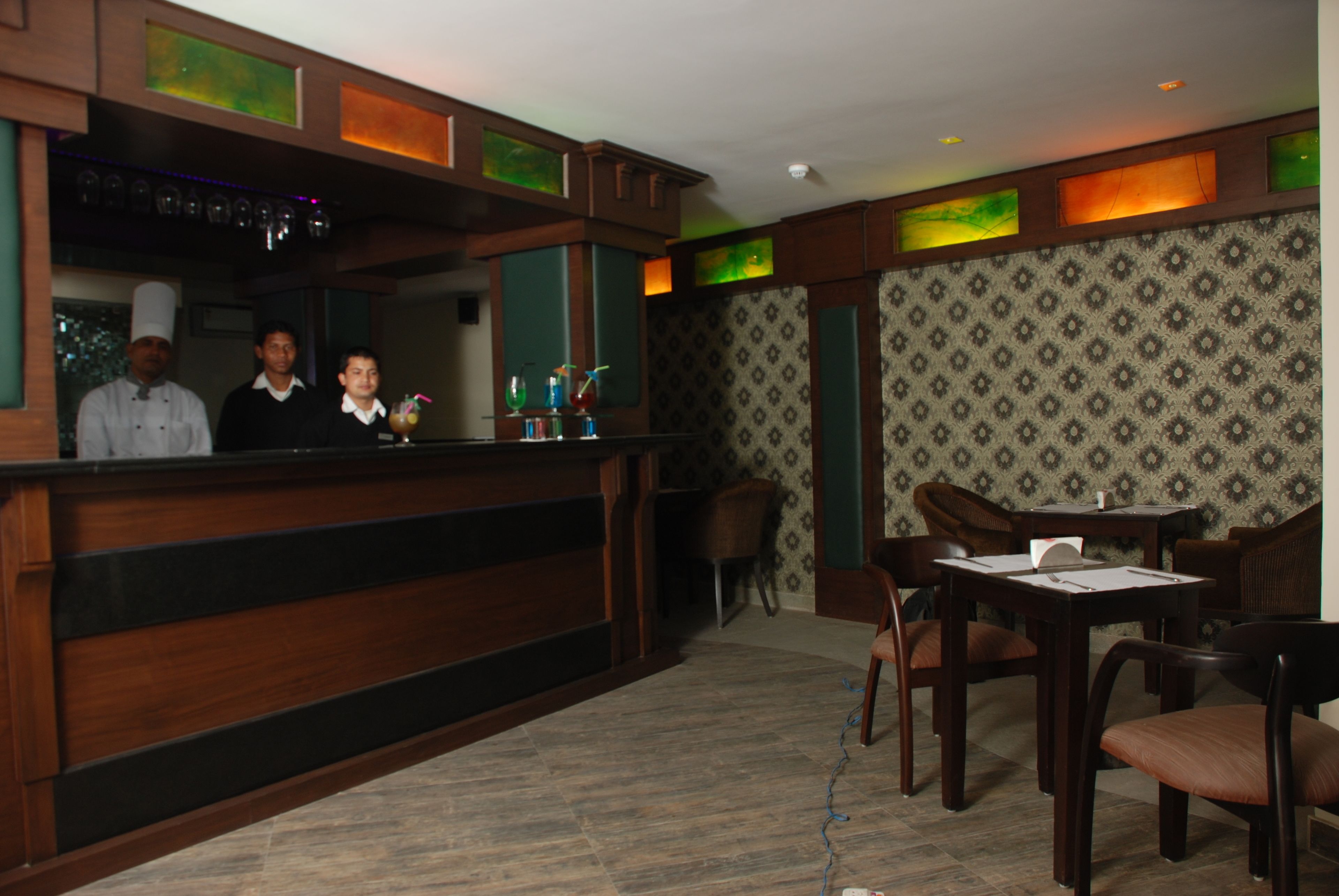 L’intérieur d’un restaurant avec un comptoir en bois, un espace bar, un papier peint à motifs et des meubles en bois.