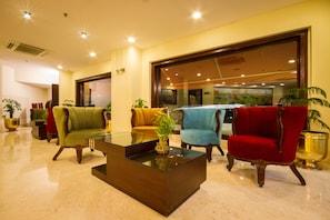 A lobby with multiple seating areas, a glass coffee table, and potted plants.