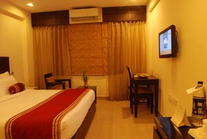 A hotel room with a bed, a desk, a chair, a television, and a water bottle.
