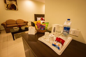 A hotel room with a sofa, a coffee table, a tray with toiletries, a basket of snacks, and a water bottle.