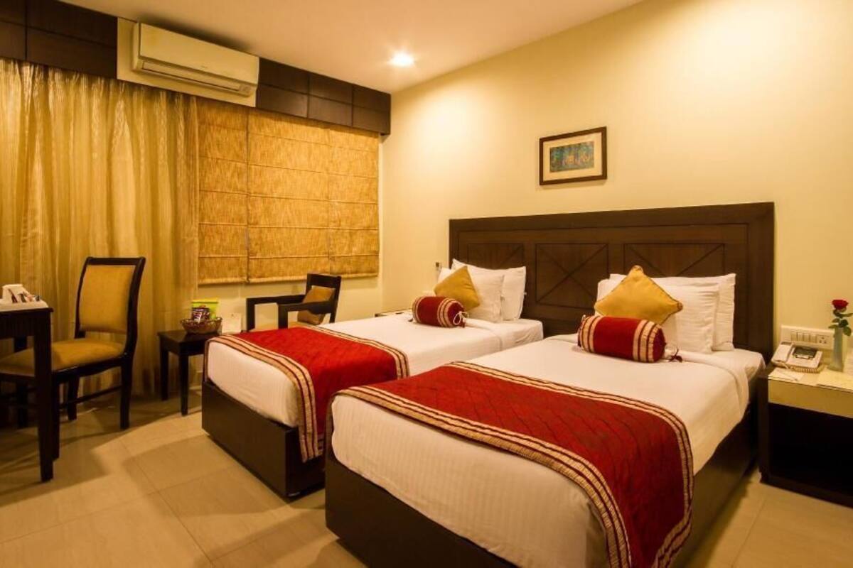 A hotel room with two beds, a desk, chairs, and a small table.