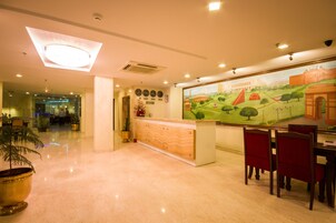 Zona de recepción de hotel con suelo de mármol pulido, un mostrador de recepción, un mural grande que representa una escena histórica y sillones tapizados en rojo.