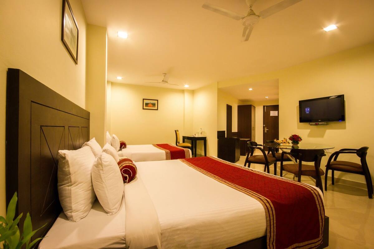 A hotel room with two beds, a desk, a chair, a television, and a ceiling fan.