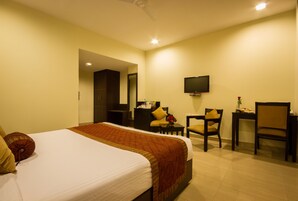 A hotel room with a bed, a desk, a chair, a television, and a small table with a vase of flowers.