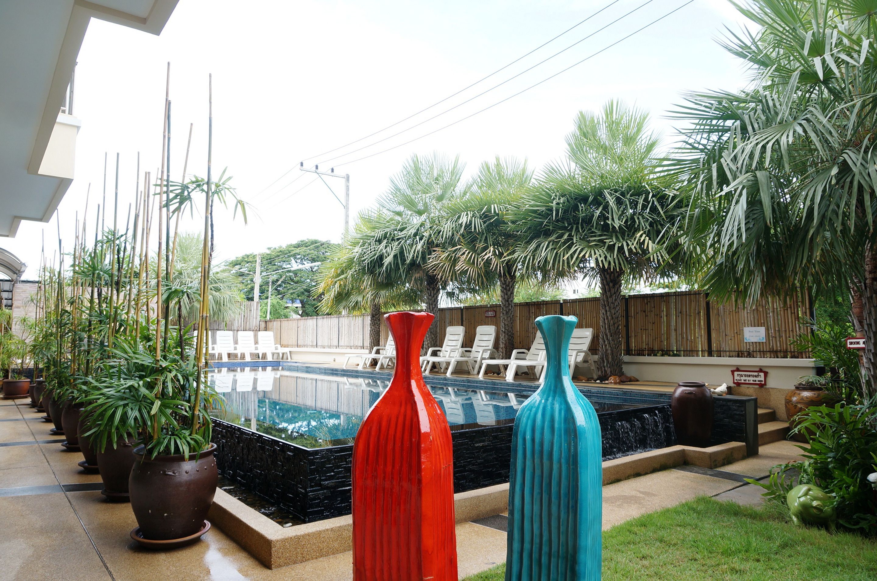 A pool area with potted plants, two large vases, and lounge chairs.