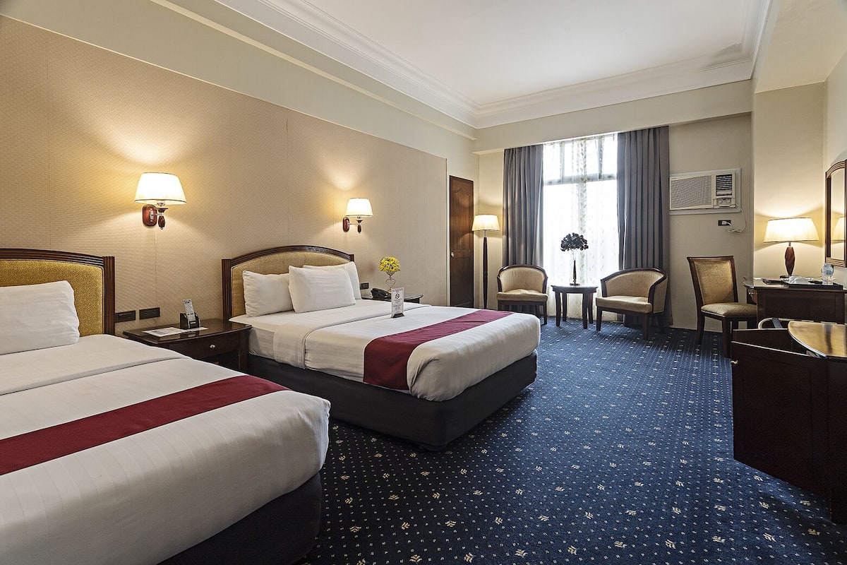 Ein Hotelzimmer mit zwei Betten, einem Schreibtisch, einem Stuhl und einem kleinen Tisch.