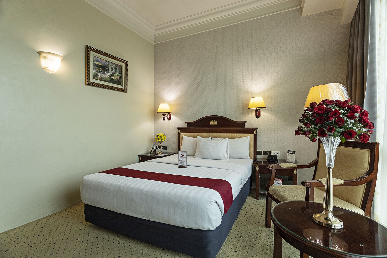 Ein Hotelzimmer mit einem Bett, Nachttischen, Lampen, einem Sessel und einer Vase mit Blumen.