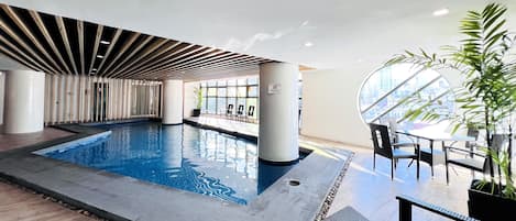 Una piscina interior con diseño moderno, rodeada de zonas de estar y grandes ventanales.