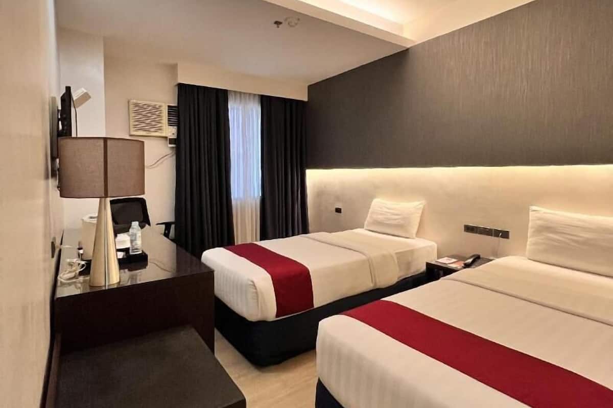 Ein Hotelzimmer mit zwei Betten, einem Schreibtisch, einem Stuhl und einem kleinen Tisch.