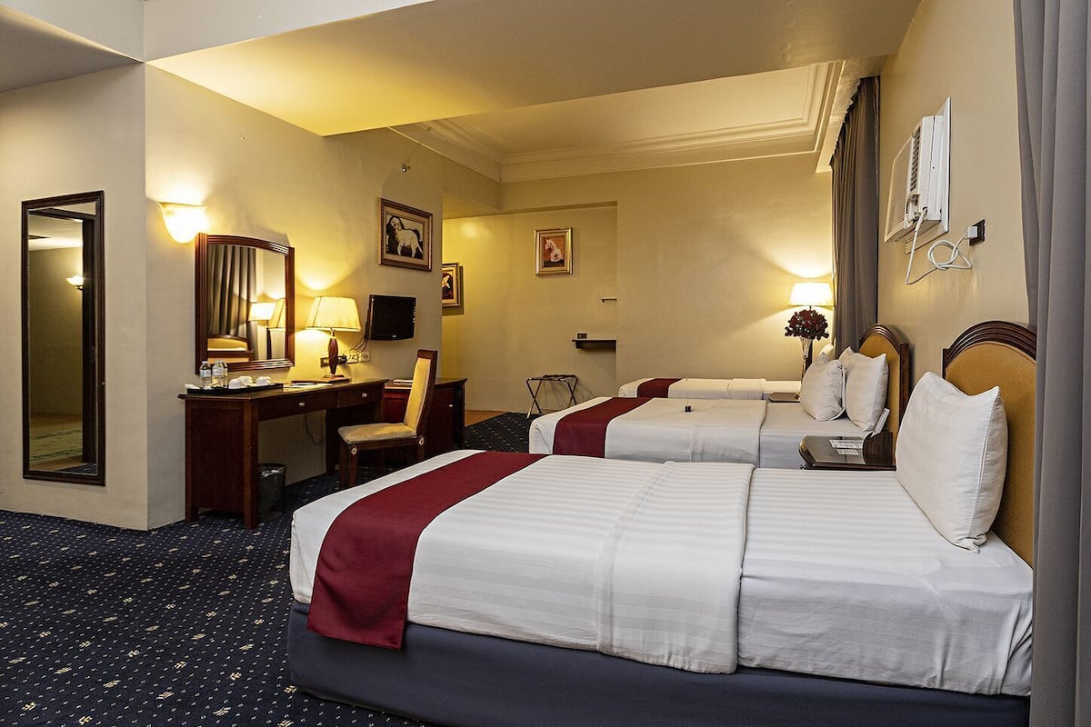 Ein Hotelzimmer mit zwei Betten, einem Schreibtisch, einem Stuhl, einem Spiegel und einem Fernseher.