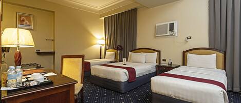 Een hotelkamer met twee bedden, een bureau met lamp, een stoel en een klein tafeltje met een dienblad.