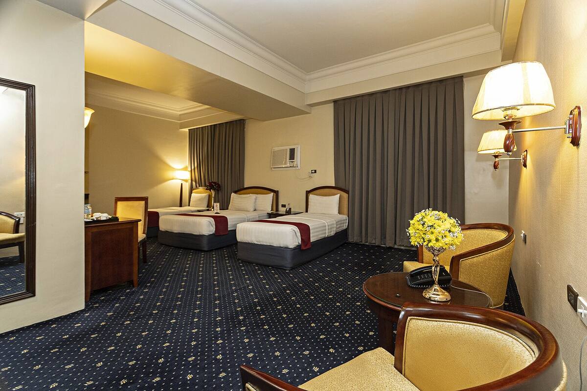 Ein Hotelzimmer mit zwei Betten, einem Schreibtisch, einem Stuhl, einer Lampe und einer Vase mit Blumen.