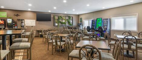 A conference room with multiple tables and chairs, a coffee station, and a large screen on the wall.