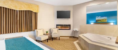 A hotel room with a large bed, a sitting area with a chair and a small table, a large bathtub, a flat-screen TV mounted on the wall, and a window with curtains.