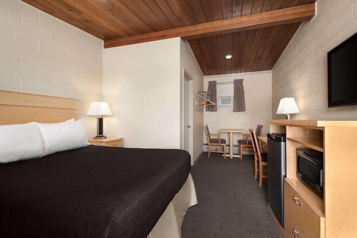 A hotel room with a bed, a desk, a chair, a television, and a microwave.