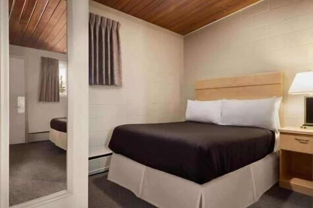 Une chambre à coucher avec un lit, une table de chevet, une lampe, une fenêtre avec des rideaux et un plafond en bois.